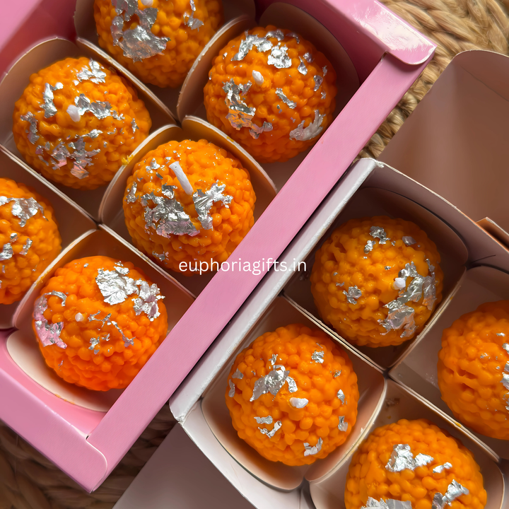 Orange candies with silver toppings in a pink box, brand 'euphorial gifts.in' visible. “Motichur laddu style candles for Diwali decoration and gifting pack of 4
