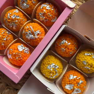 Orange and yellow textured candles with silver decorations in a pink box.