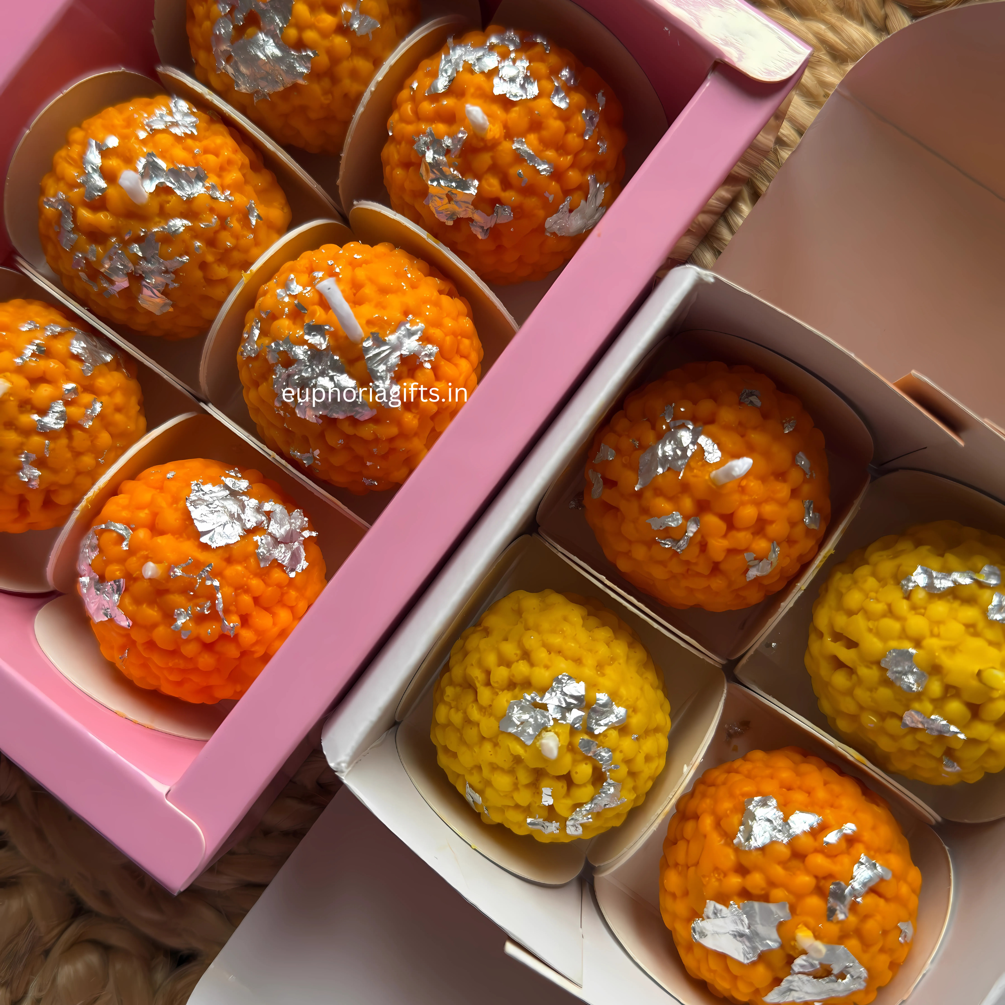Orange and yellow textured candles with silver decorations in a pink box.