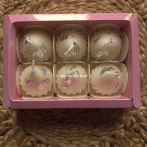 Beautifully packed modak soy candles in mithai-style gift box Set of six small candles in a pink box on a woven surface