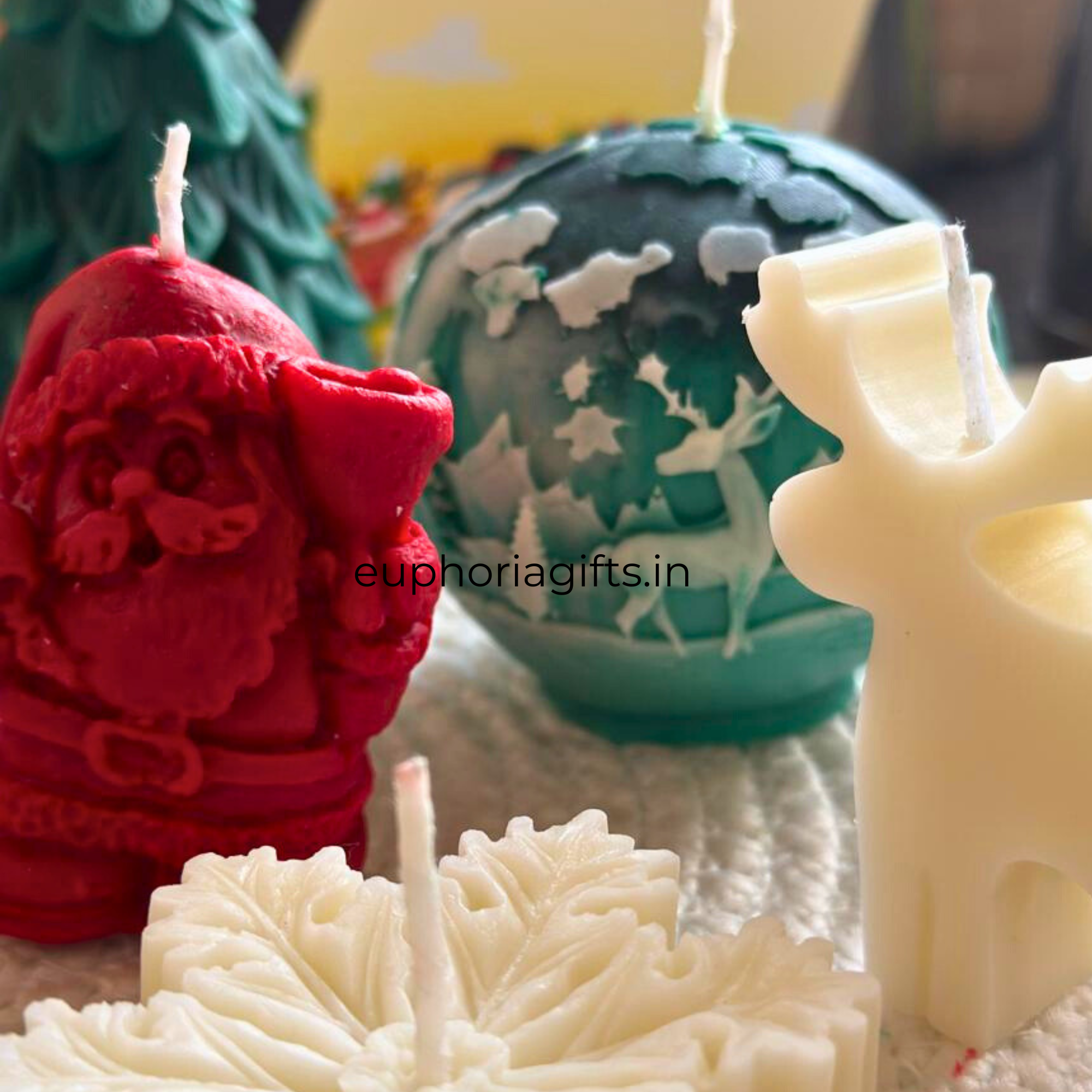 Decorative candles shaped like a Santa Claus, reindeer, and Christmas tree on a textured surface.