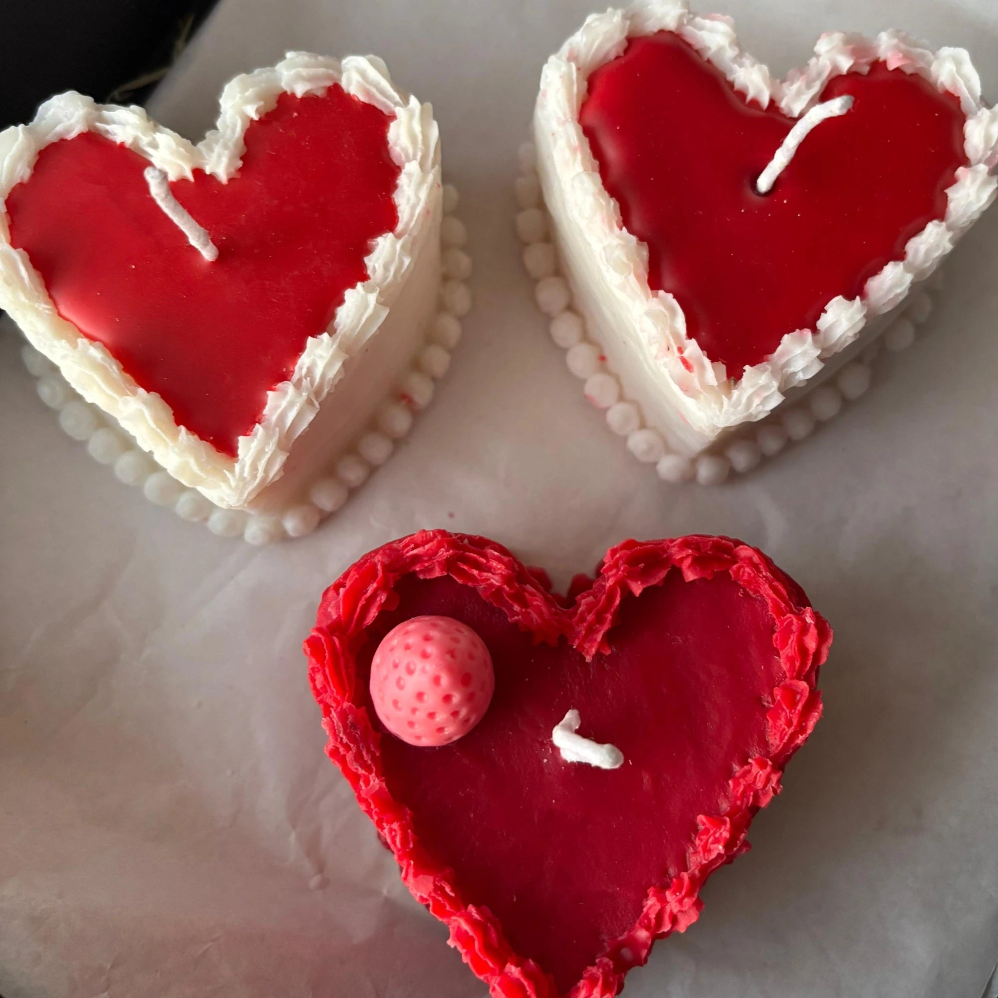 Flatlay of three heart cake candles, two white with red centers and one fully red with a pink ball topping.