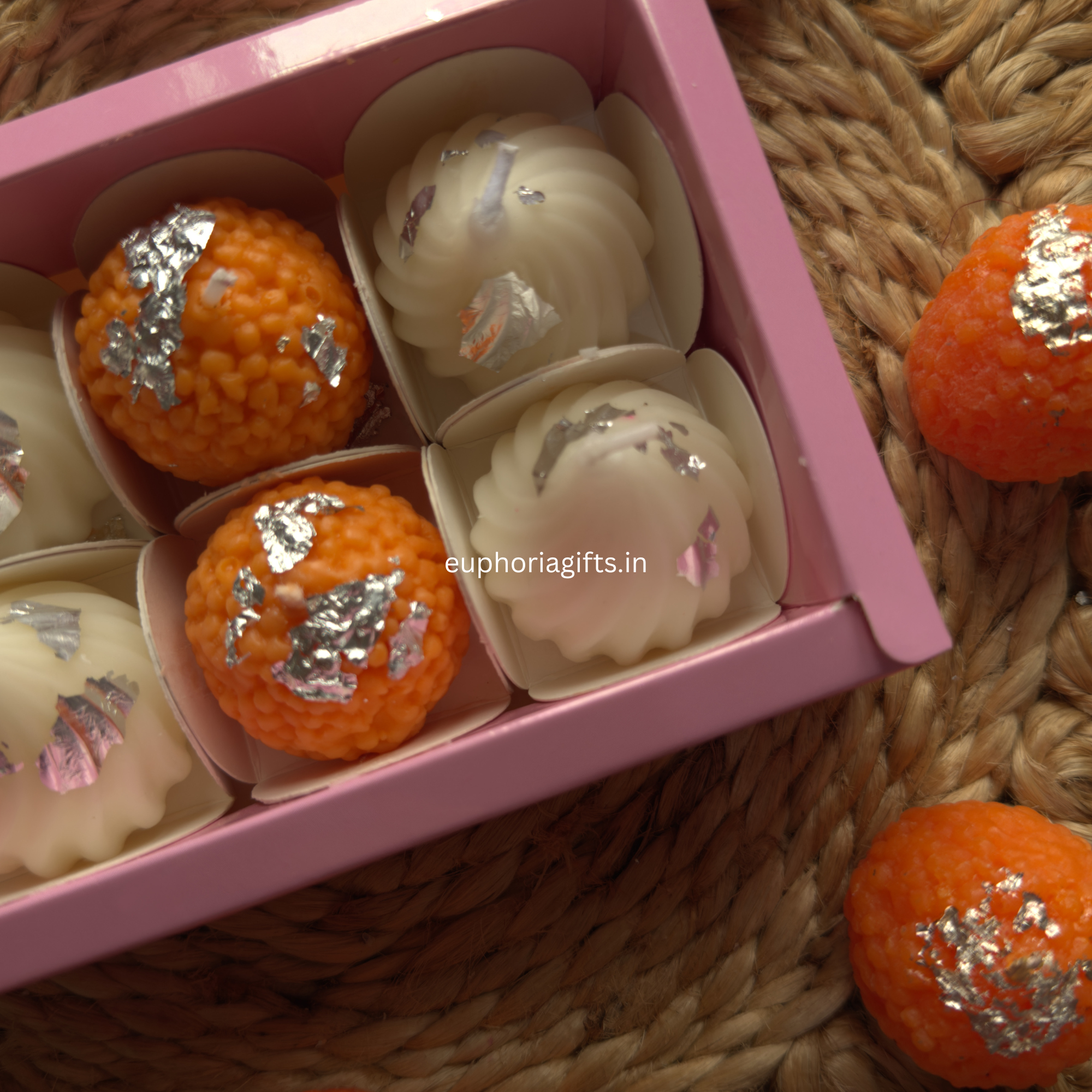 “Indian mithai-inspired candles for spiritual home decor Decorative items in a pink box on a woven surface with 'euphoriagifts.in' laddo candle branding.