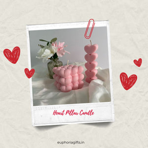 Pink heart pillar and cube candles styled with artificial flowers, captured in a Polaroid frame for a Valentine’s gift aesthetic. Heart-shaped pillar candles with a decorative paper clip on a light background, featuring the brand 'euphoriagifts.in'.