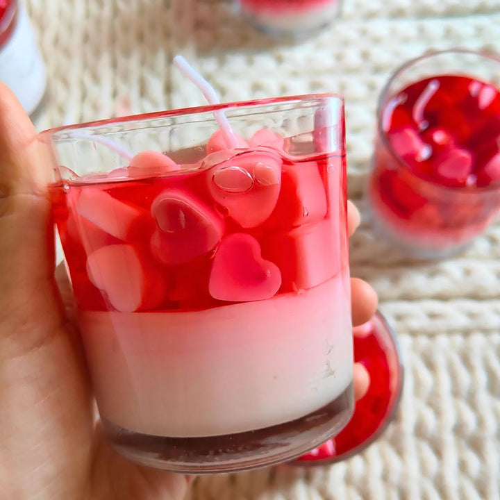 Hand holding a heart-shaped gel wax candle in a clear glass jar with red and pink layers