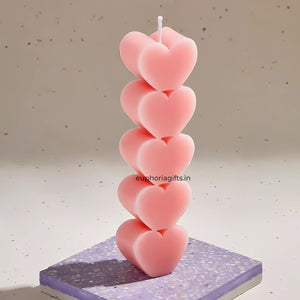 Stack of pink heart-shaped candles on a textured surface with 'euphoriagifts.in' branding. Single pink heart pillar candle displayed on a terrazzo base, highlighting its detailed design and soft finish