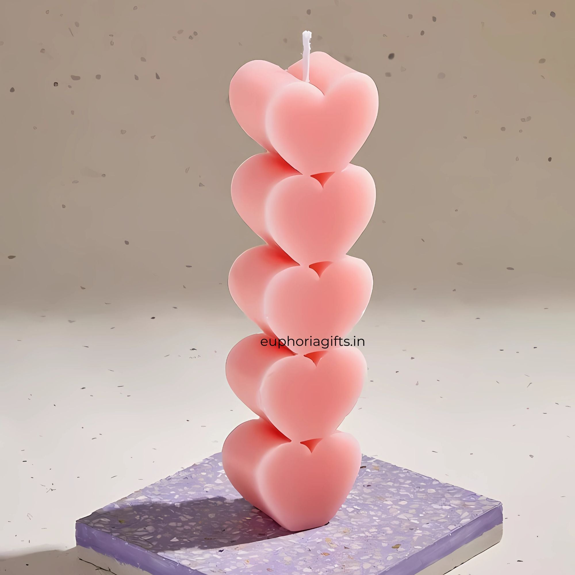 Stack of pink heart-shaped candles on a textured surface with 'euphoriagifts.in' branding. Single pink heart pillar candle displayed on a terrazzo base, highlighting its detailed design and soft finish