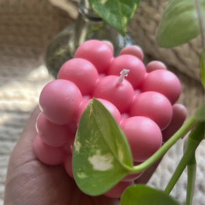 pink bubble candle made from natural soy wax, placed on a wooden coaster with pinecones in the background, highlighting features like long-lasting burn and relaxing ambiance.

