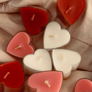 Heart-shaped candles in red, pink, and white on a beige fabric background.